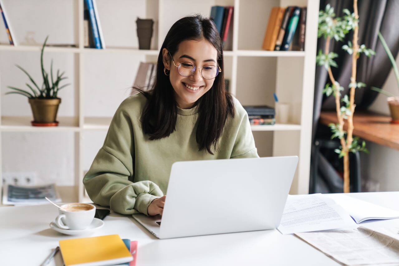 a happy woman using a laptop on a white desk